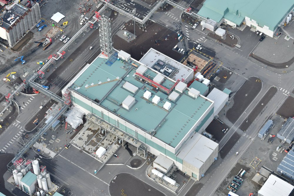 Aerial view of large industrial nuclear waste treatment facility, large stack coming out of roof, roads, piping around building.