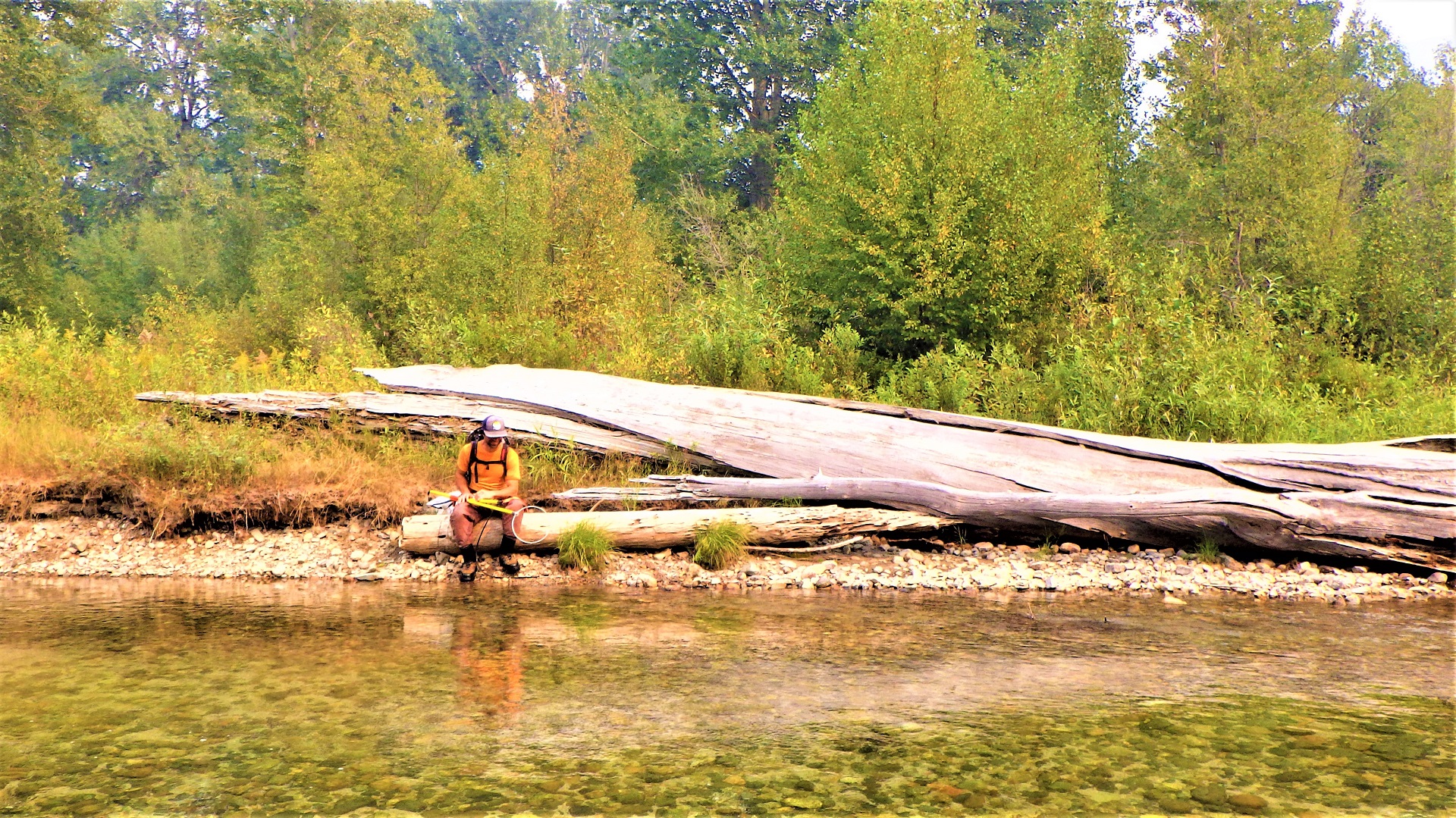 A person with a backpack electrofisher sitting on the bank of a river