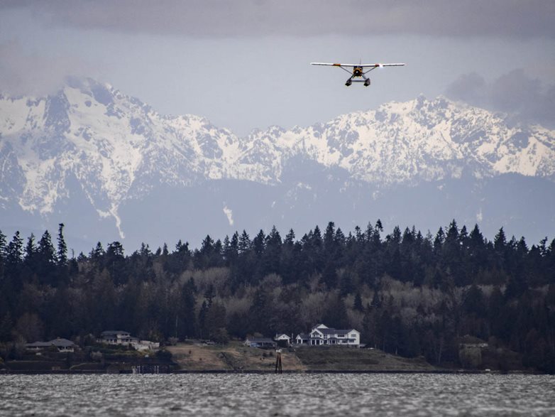 Seaplane coming in for a landing on the water with mountains in the background.